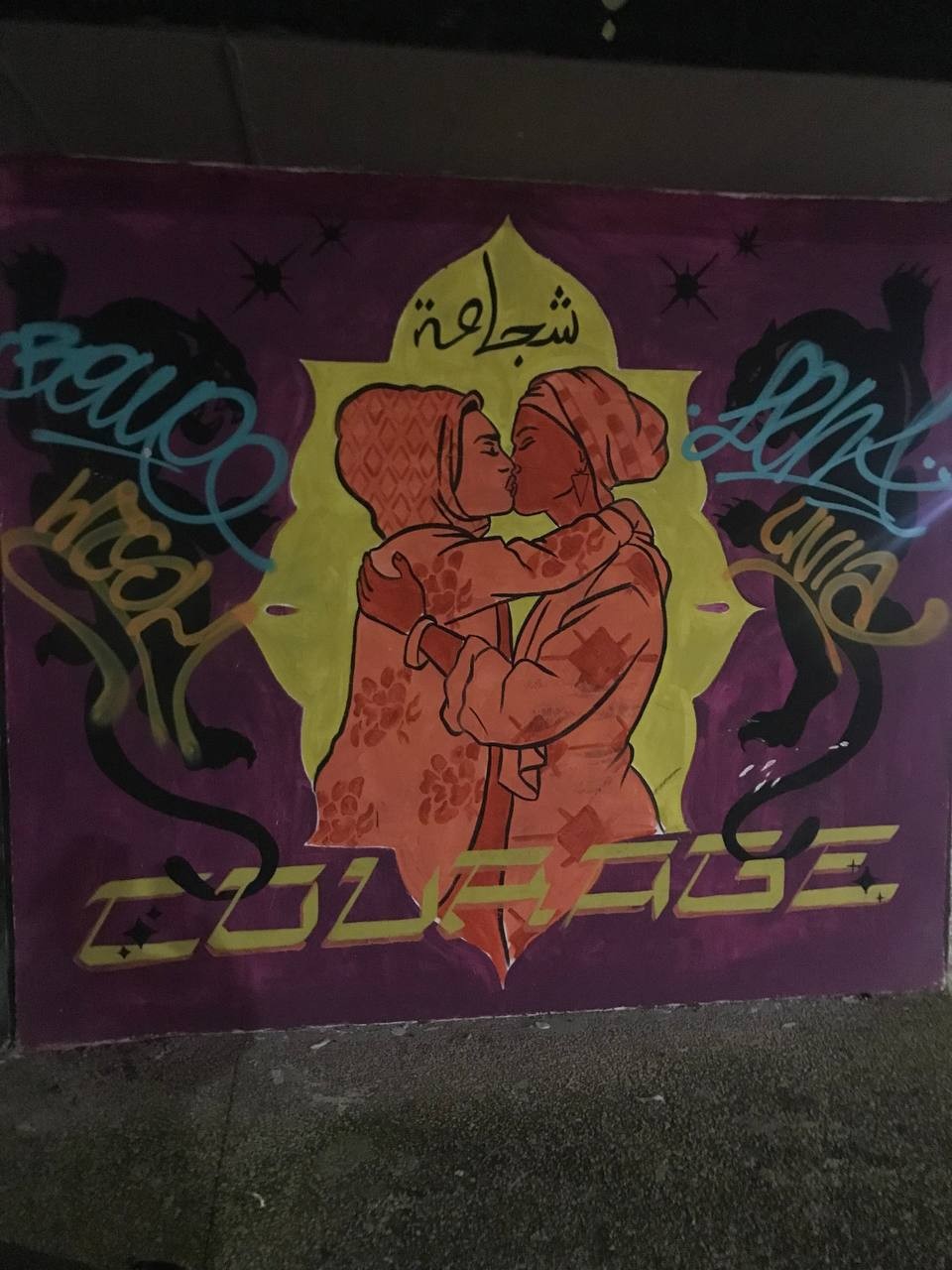 Street art depicting 2 women kissing. Above their heads, in Arabic is written Courage. Below them, it is written courage in English
